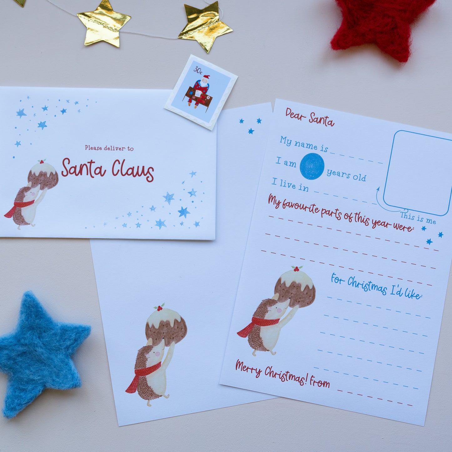 A flat-lay of a Christmas letter writing set featuring a Santa Claus stamp and pudding illustration, including a letterhead and envelope 